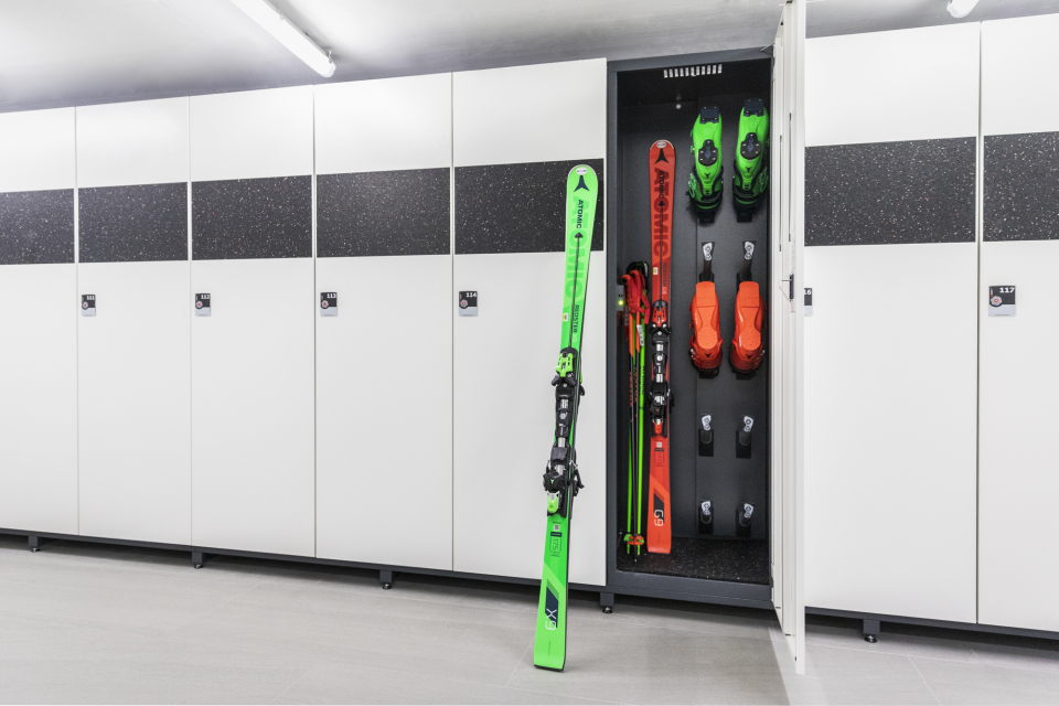 Ein grüner und ein roter Ski und dazu farbig passende Skischuhe stehen im Skidepot.