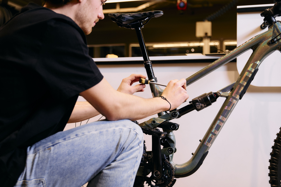 Eine Person in schwarzem Hemd und Jeans stellt in einer Werkstatt die Sattelstütze eines Fahrrads ein.